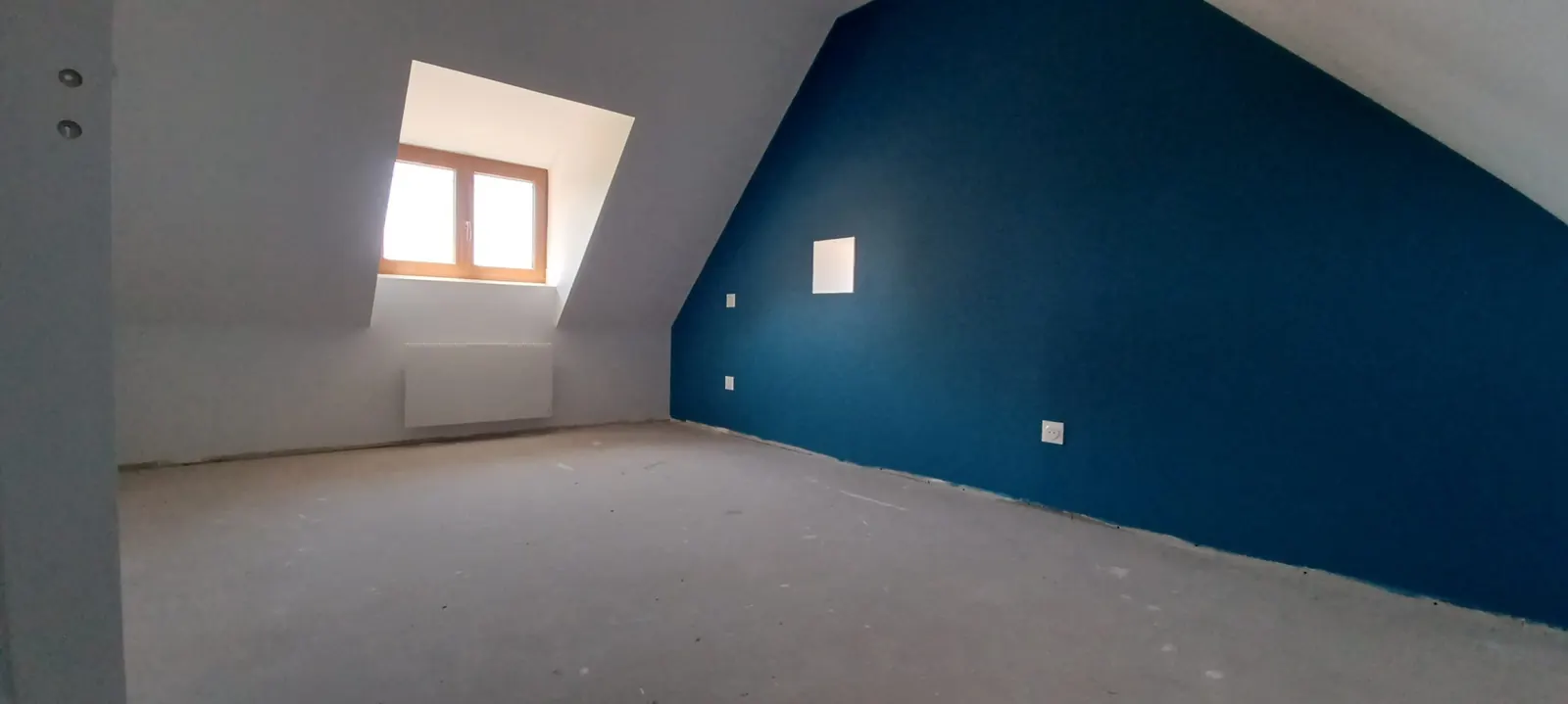 Combles aménagés avec un mur peint en bleu et une fenêtre de toit