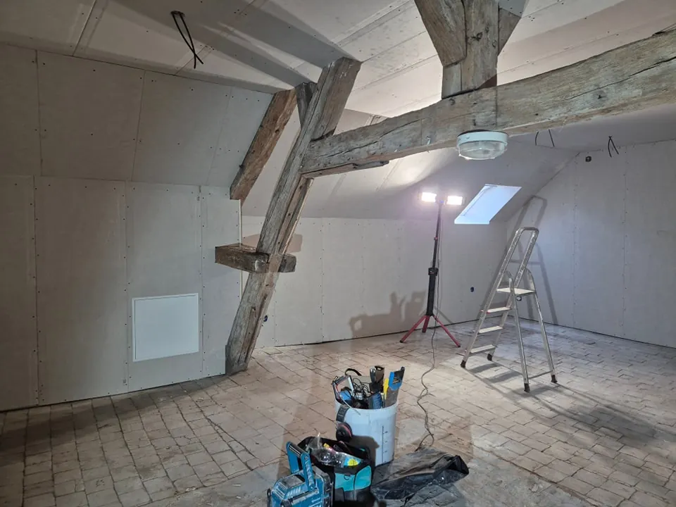 Combles aménagés : plaques de plâtre posées autour des poutres apparentes, chantier en cours
